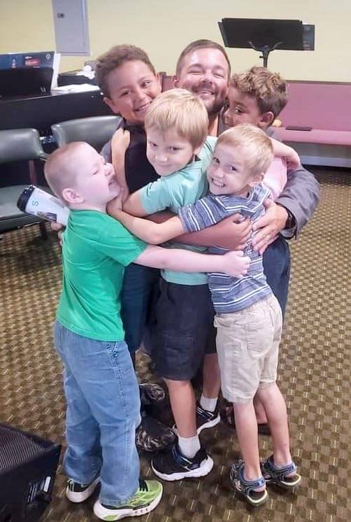 Children of apostolic church hugging pastor and smiling.